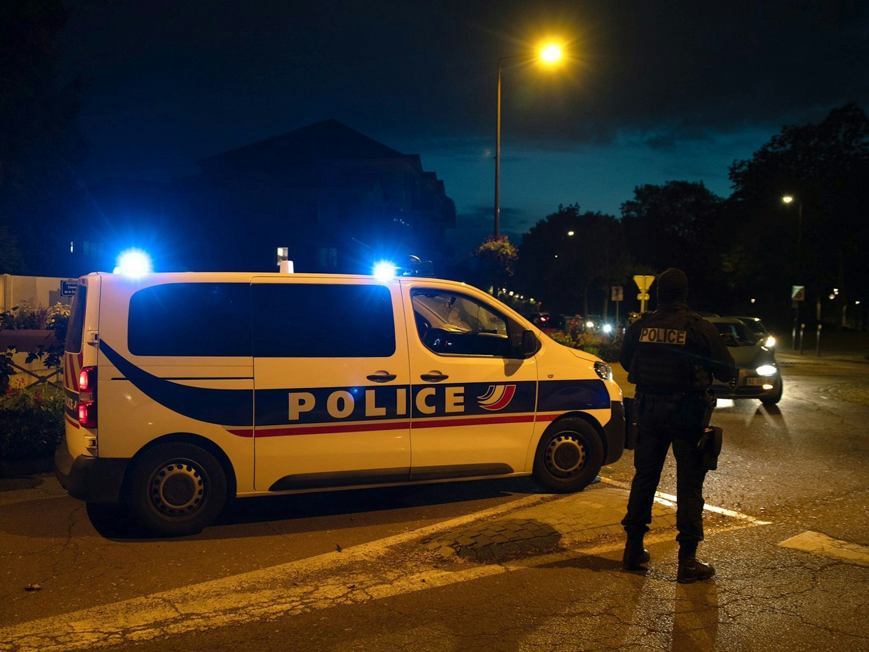 Französisches Polizeiauto steht nachts auf der Straße, daneben ein französischer Polizist. Symbolbild vom 16. Oktober 2020.