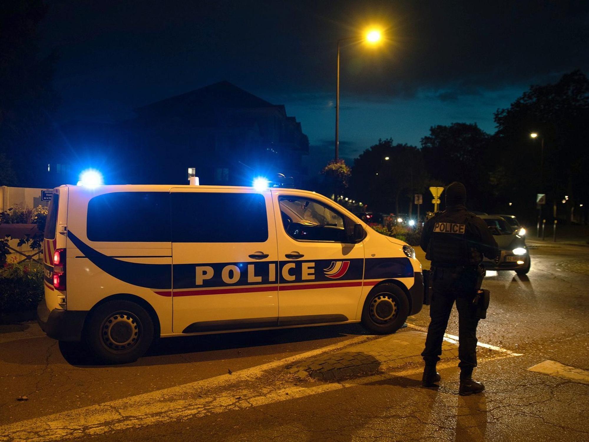 Französisches Polizeiauto steht nachts auf der Straße, daneben ein französischer Polizist. Symbolbild vom 16. Oktober 2020.