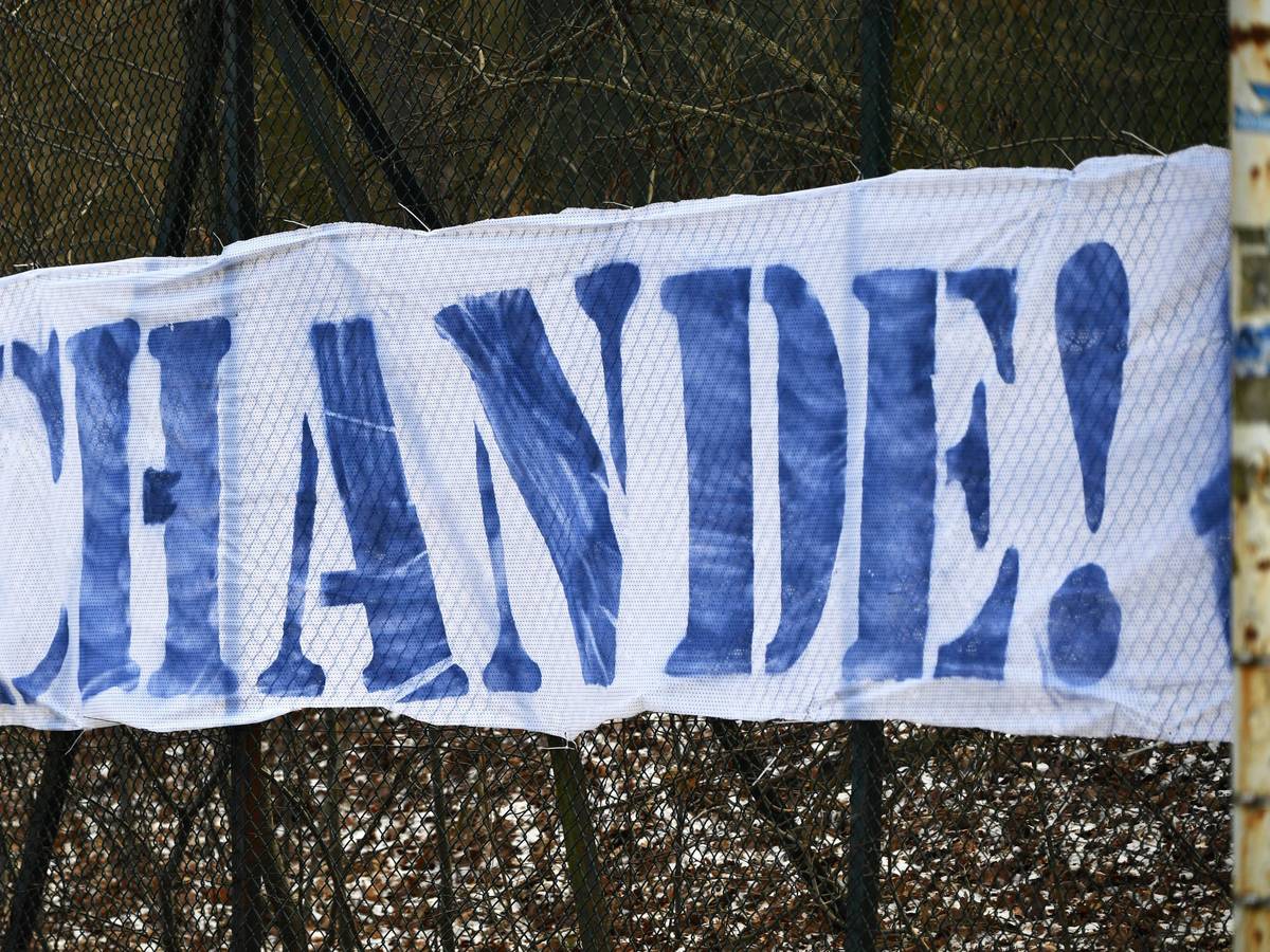 Ein weißes Banner mit der Aufschrift „Schande“ in blauen Buchstaben ist zu lesen.