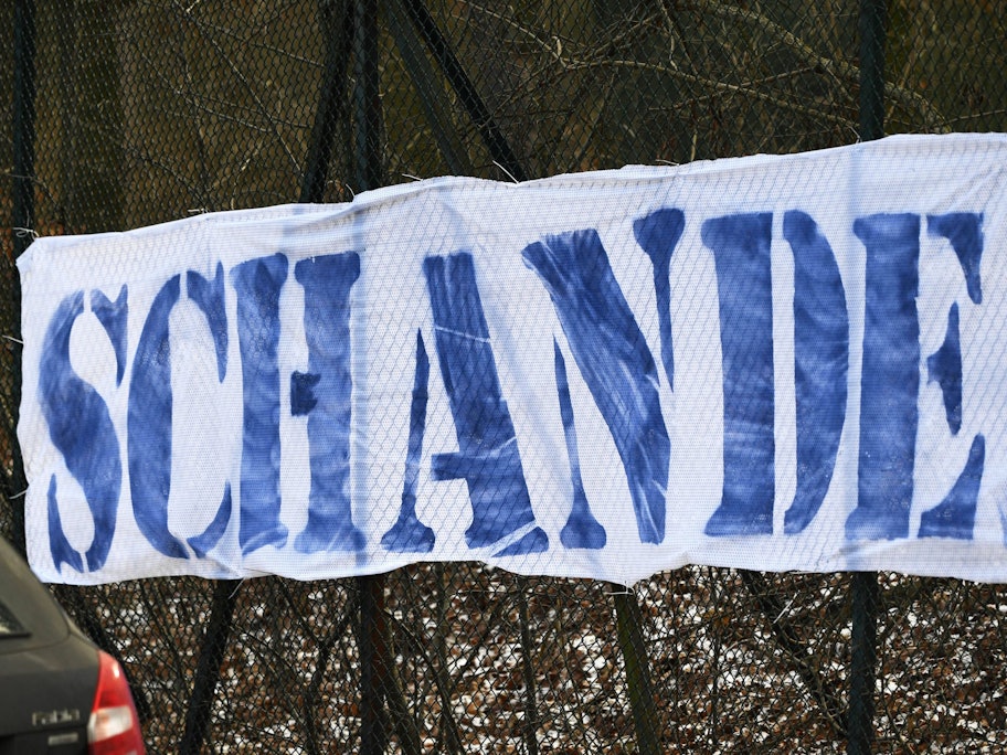 Ein weißes Banner mit der Aufschrift „Schande“ in blauen Buchstaben ist zu lesen.