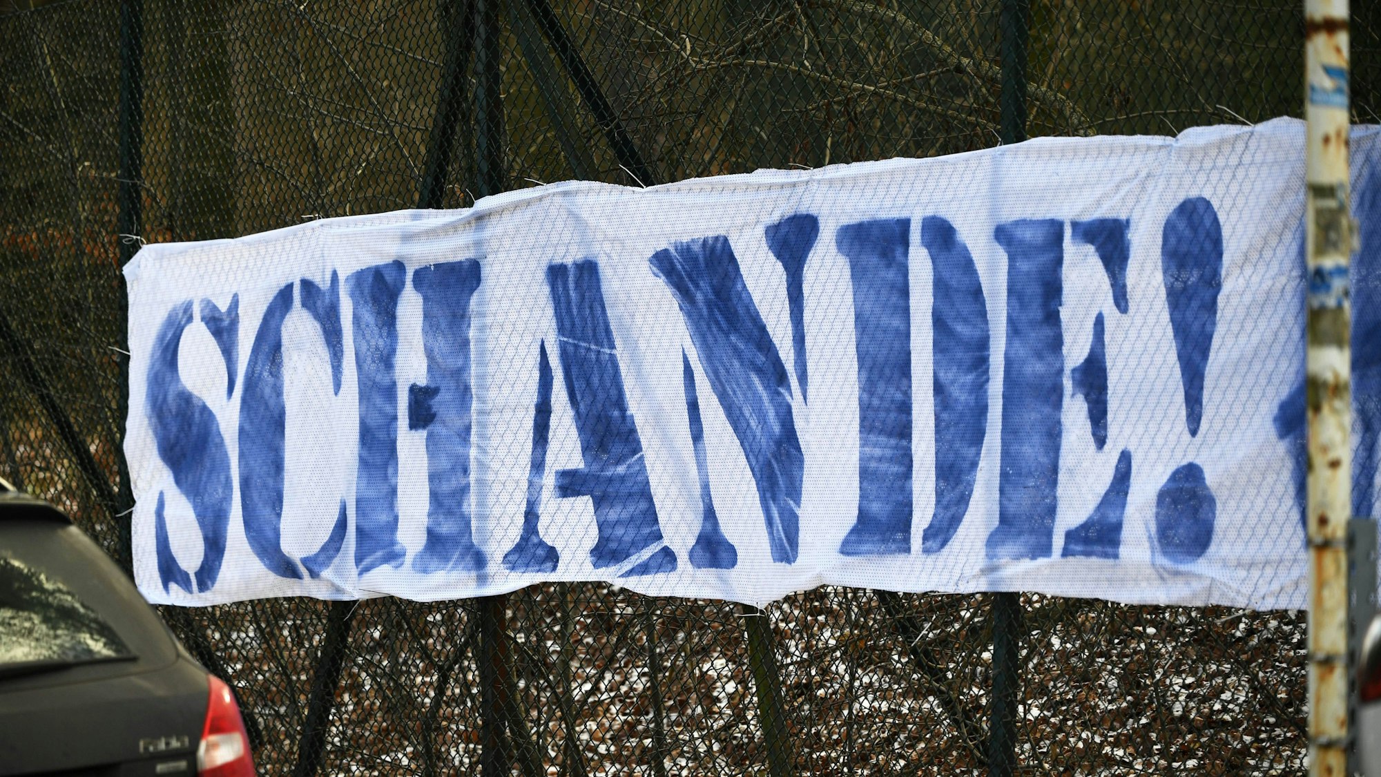 Ein weißes Banner mit der Aufschrift „Schande“ in blauen Buchstaben ist zu lesen.