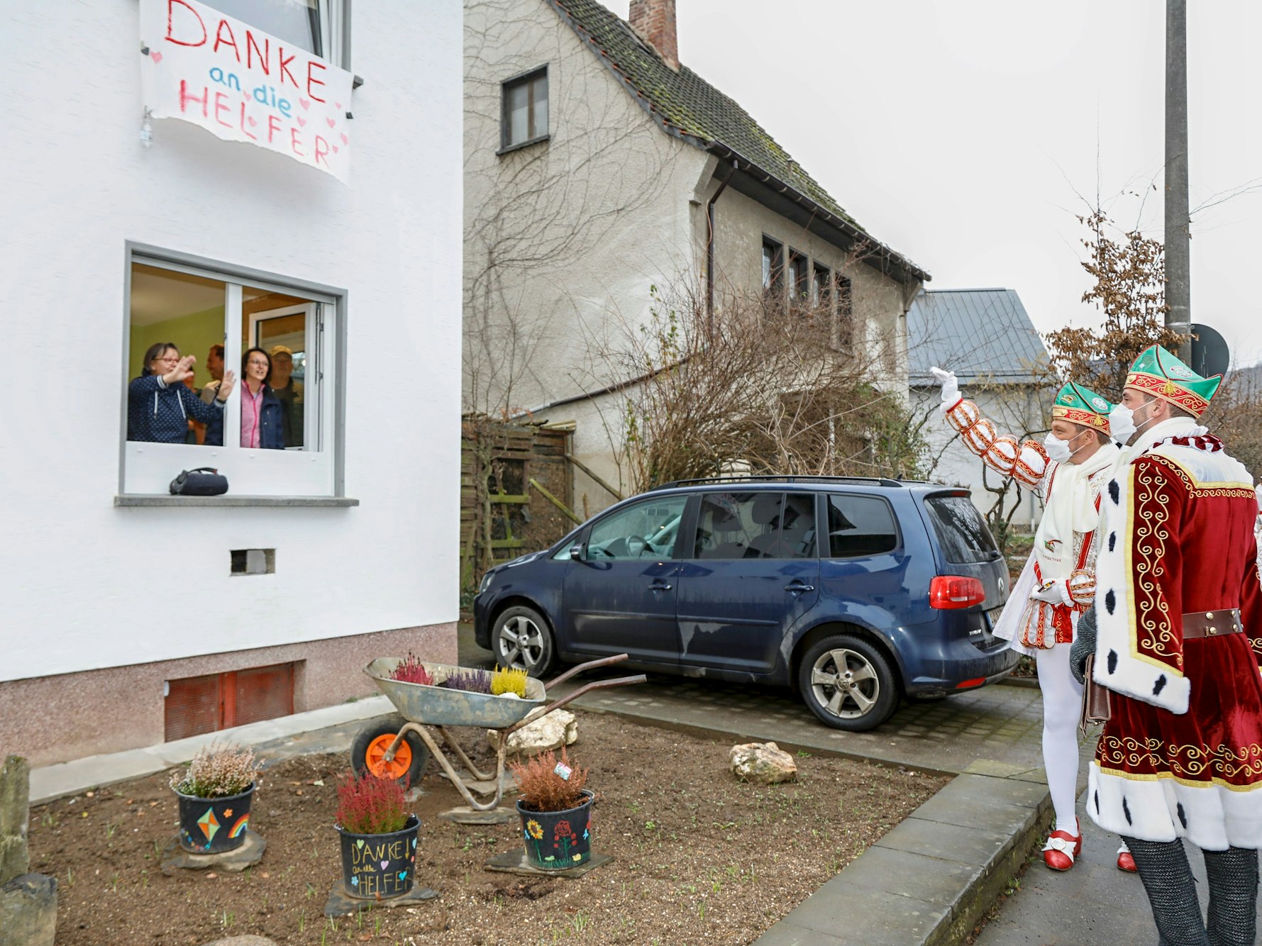 Menschen schauen aus dem Fenster und begrüßen das Dreigestirn auf der Straße.
