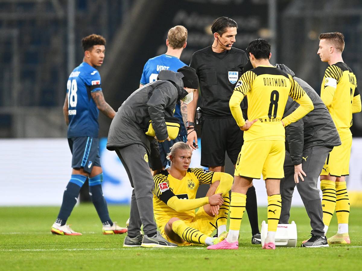 Erling Haaland sitzt auf dem Boden, hinter ihm stehen Mitspieler Marco Reus und Schiedsrichter Deniz Aytekin.