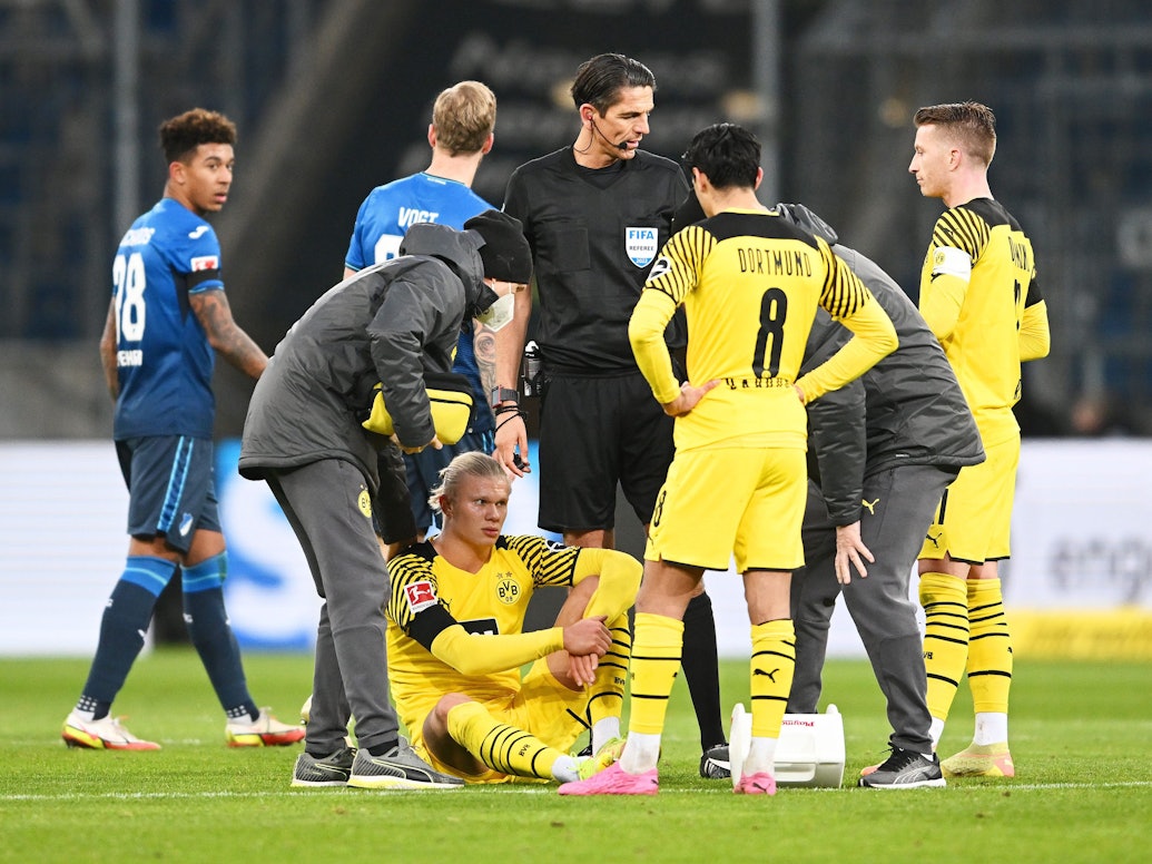 Erling Haaland sitzt auf dem Boden, hinter ihm stehen Mitspieler Marco Reus und Schiedsrichter Deniz Aytekin.