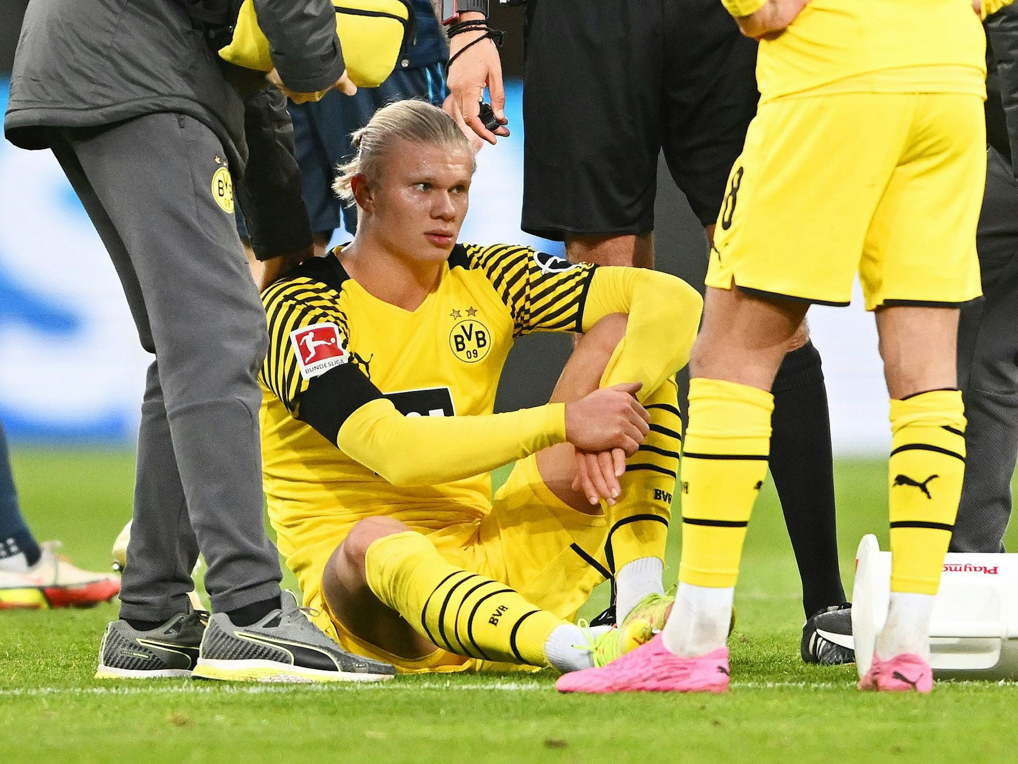 Erling Haaland sitzt auf dem Boden, hinter ihm stehen Mitspieler Marco Reus und Schiedsrichter Deniz Aytekin.