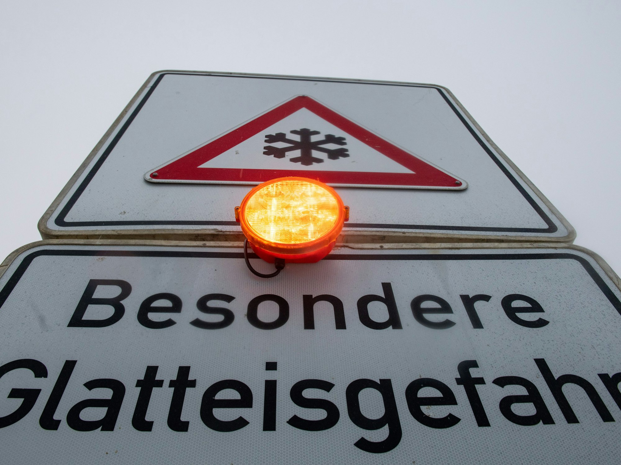 Ein Straßenschild warnt mit einer Blinkleuchte vor Glatteis.