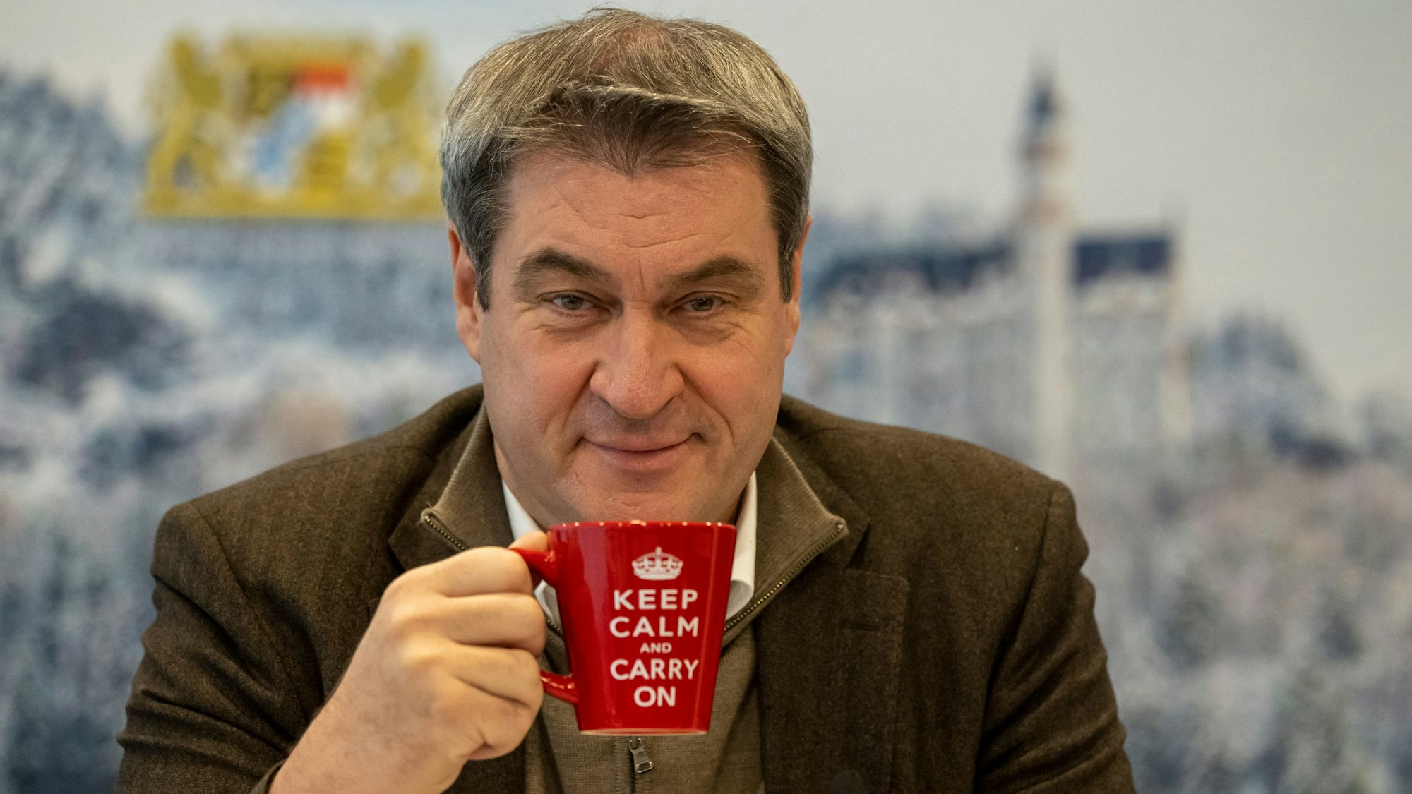 Markus Söder (CSU), Ministerpräsident von Bayern, sitzt vor Beginn einer Online-Sitzung des bayerischen Kabinetts an seinen Platz vor einer winterlichen Fotowand.