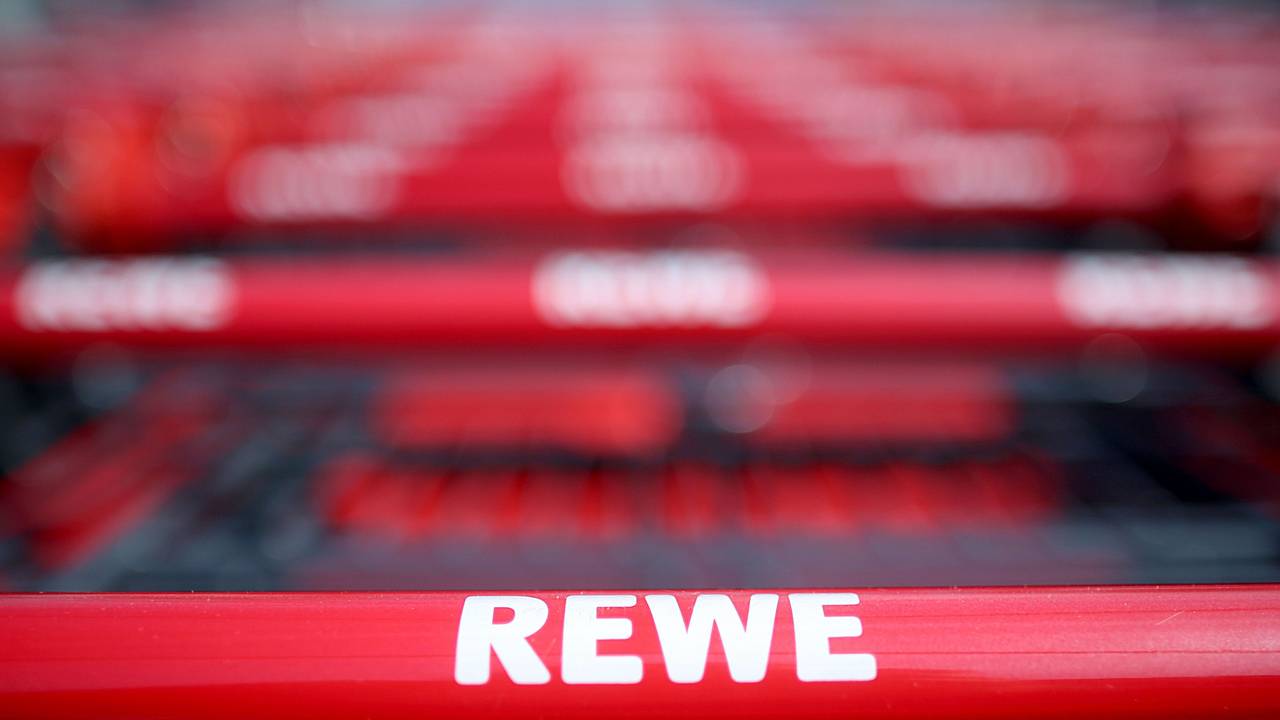 Einkaufswagen stehen vor einem Rewe Supermarkt.