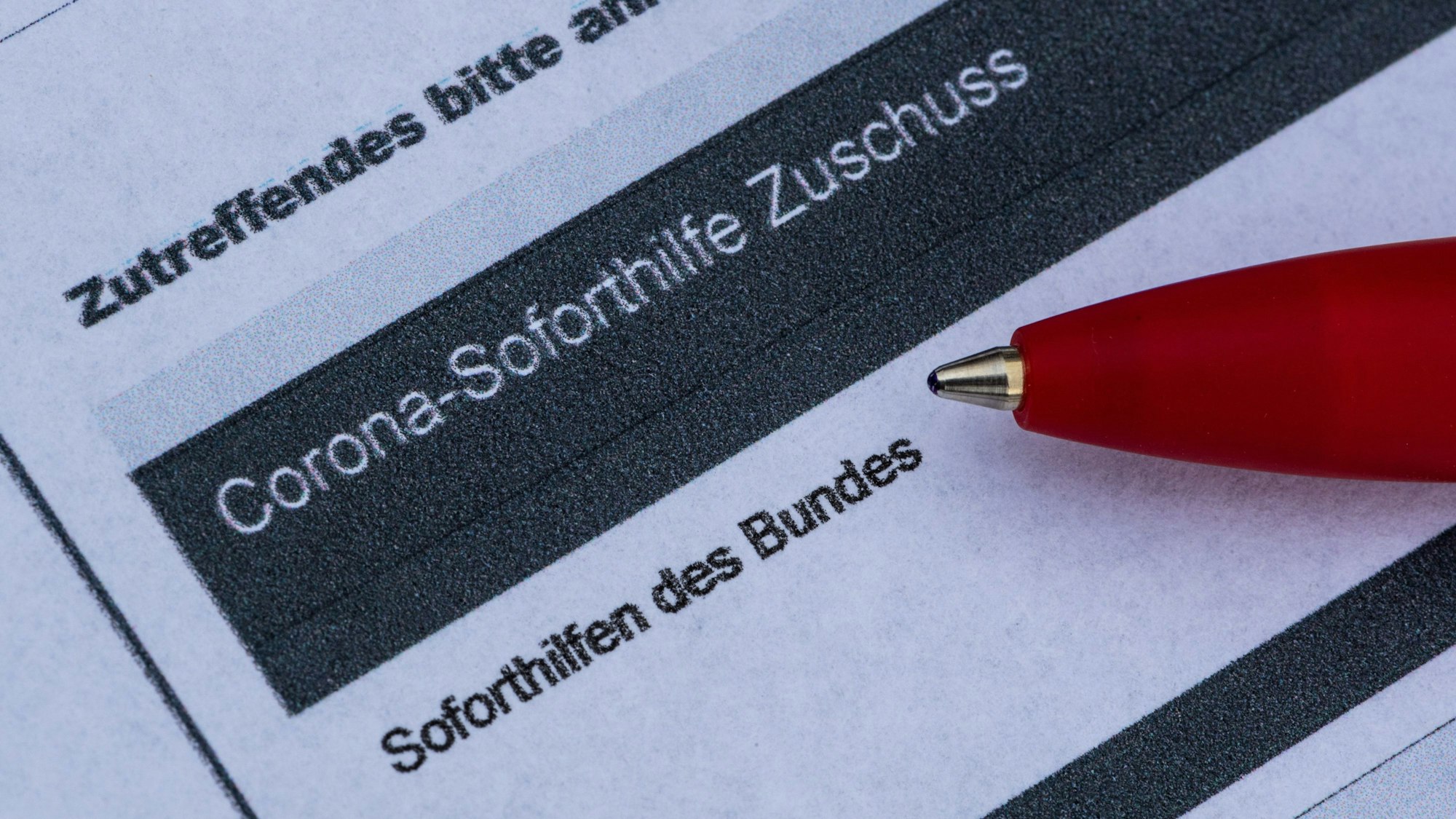 Ein Stift liegt auf einem Antrag für den Corona-Soforthilfe-Zuschuss.