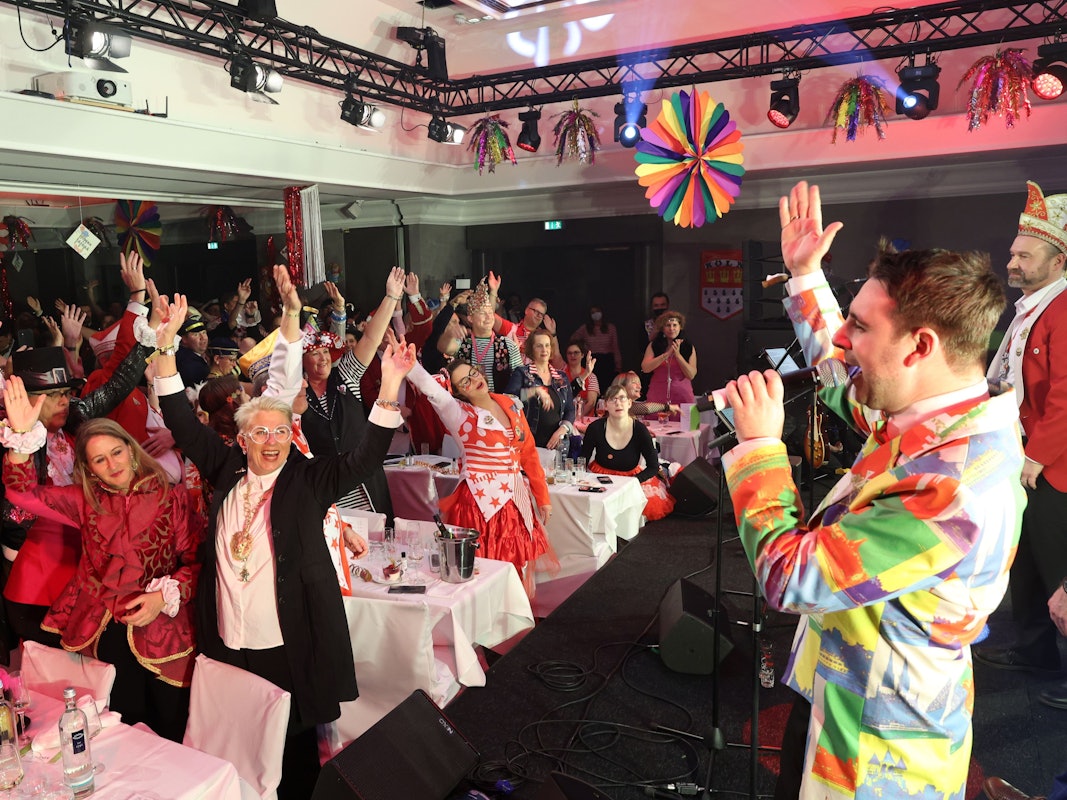 Tanzendes und mitsingendes kostümiertes Publikum in einem Saal.