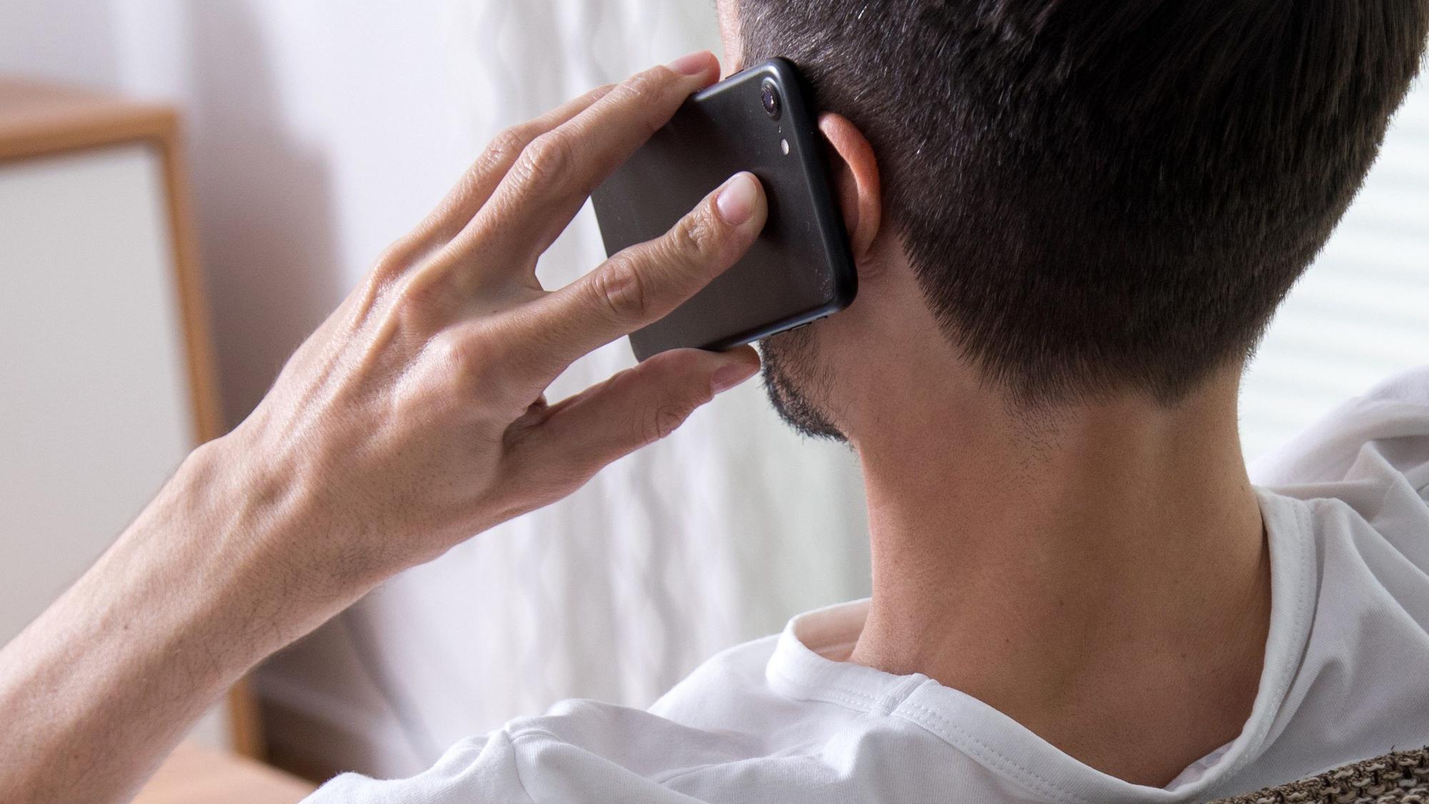 Ein Mann telefoniert mit seinem Handy am linken Ohr.