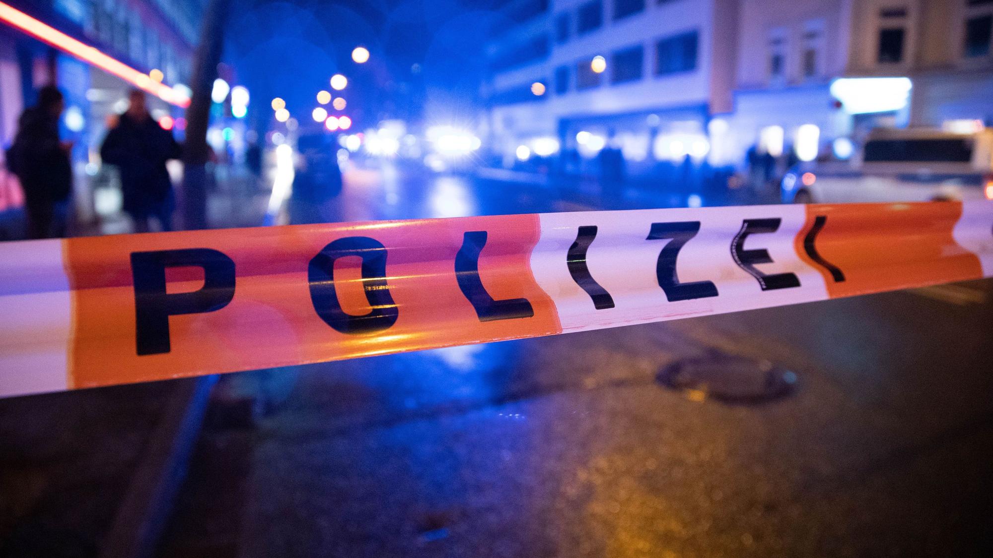 Ein Polizei-Absperrband ist über eine Straße gespannt, auf der eine Menschengruppe marschiert.