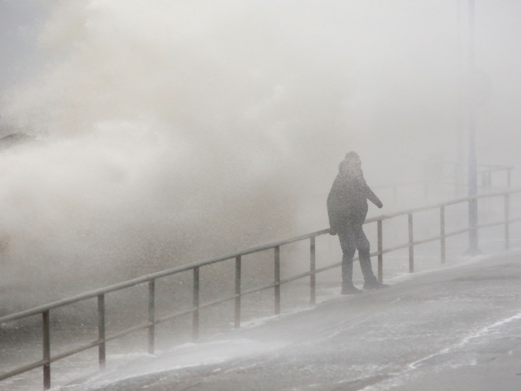 Meterhoch spritzt das Wasser bei starkem Sturm auf die Mole des Fähranlegers Dagebüll, wo ein Passant gerade verweilt.