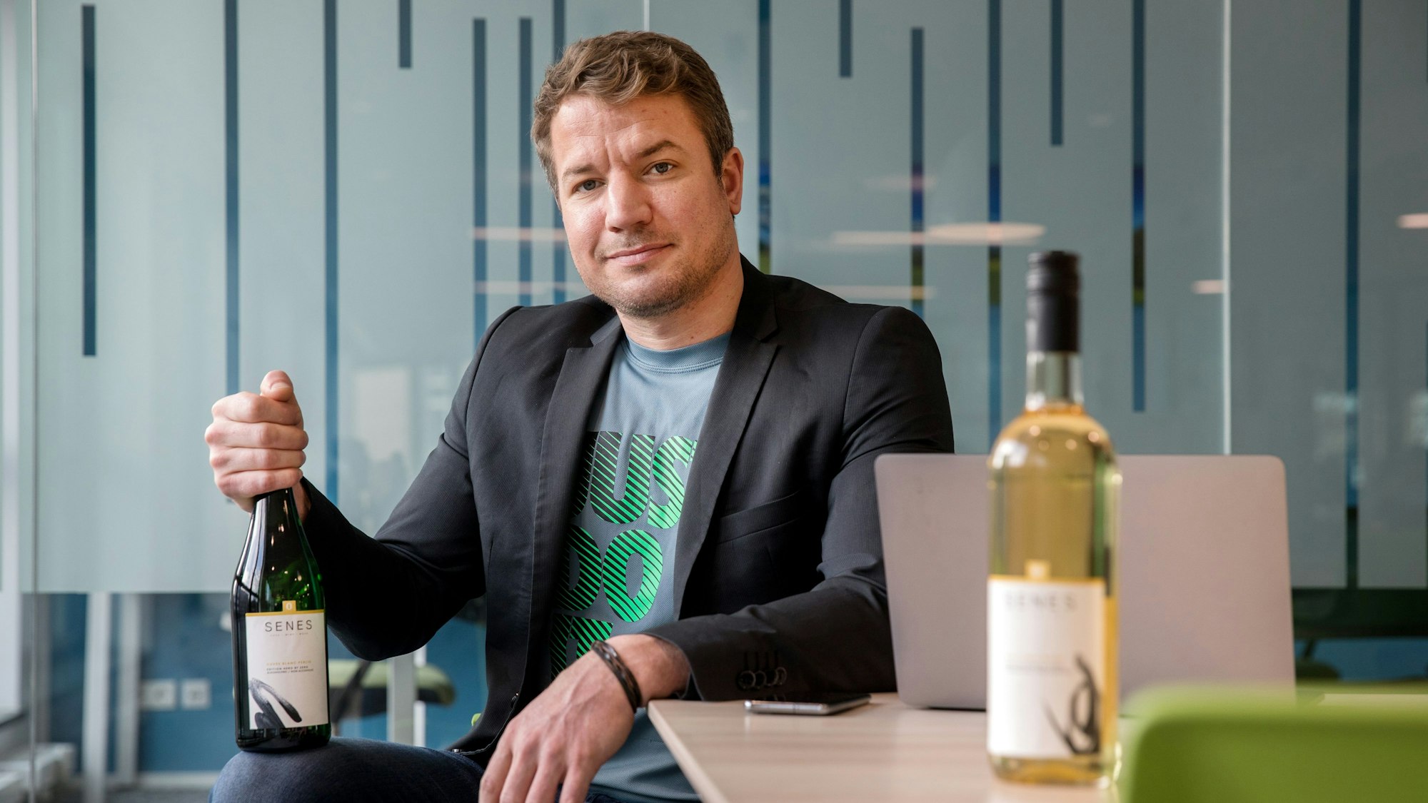 Der Kölner Christian Huettl sitzt mit zwei seiner alkoholfreien Weine am Tisch.