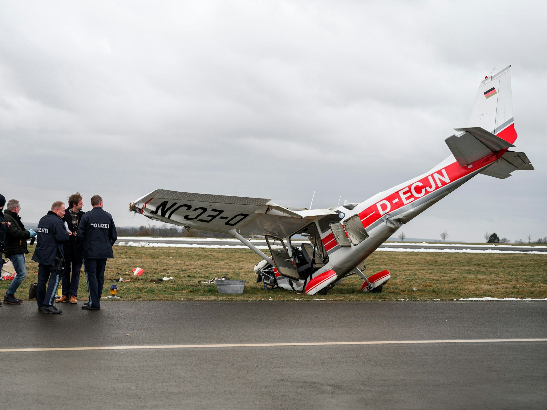 Die ermittelnden Polizeibeamten stehen am 28. Januar 2022 neben dem verunglücktem Flugzeug des Herstellers Cessna. Ein Kleinflugzeug ist mit zwei Insassen, einem Fluglehrer und einem Flugschüler am Flugplatz Coburg-Brandensteinsebene verunglückt.