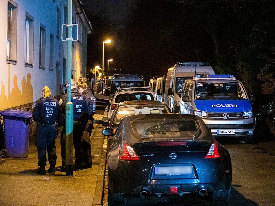Einsatzkräfte der Polizei sowie mehrere Polizeifahrzeuge stehen vor einem Haus.