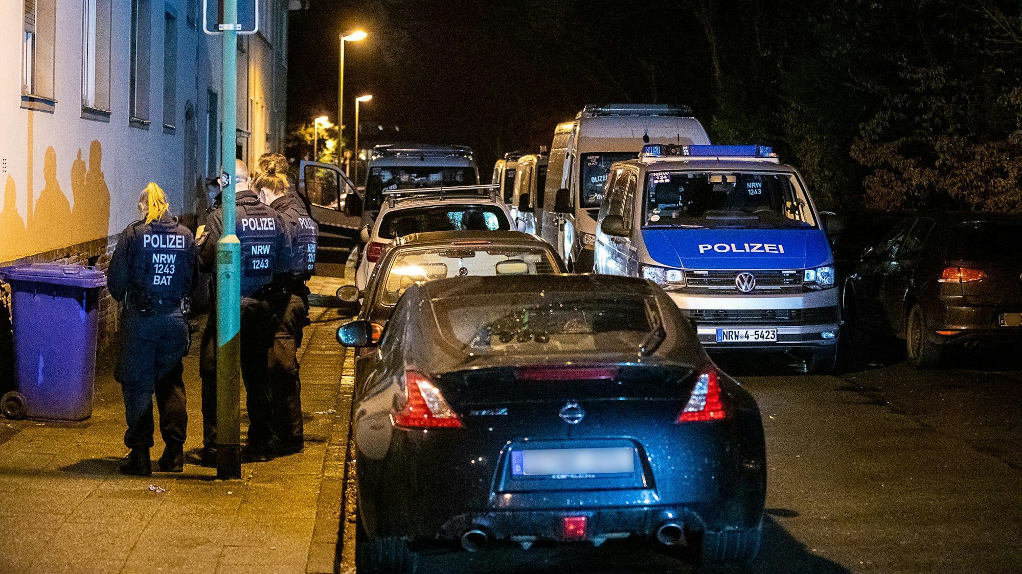 Einsatzkräfte der Polizei sowie mehrere Polizeifahrzeuge stehen vor einem Haus.