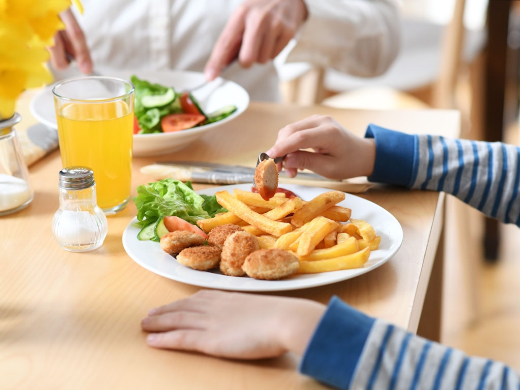 Ein Junge sitzt vor einem Teller mit Chicken Nuggets und Pommes Frites.