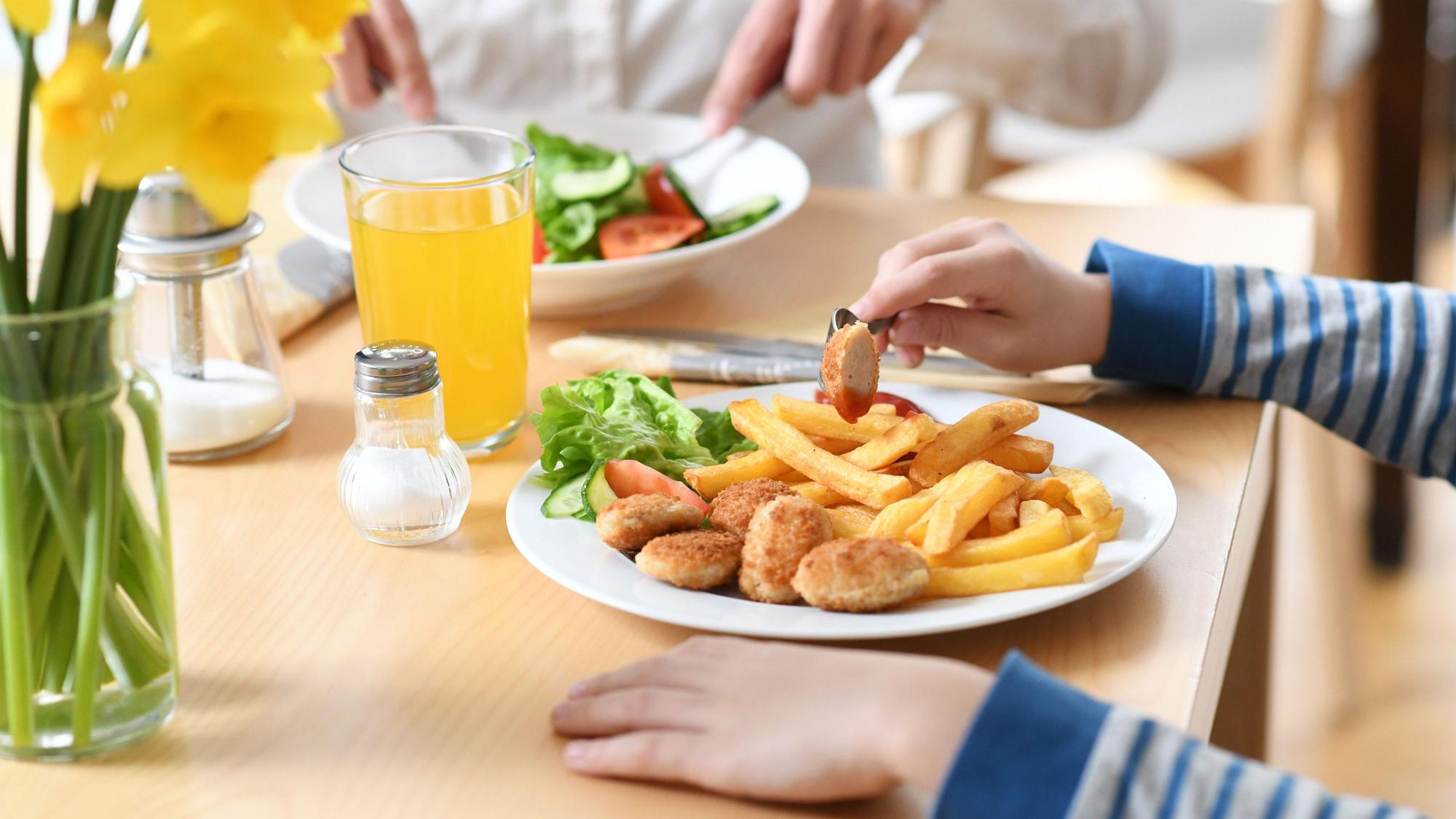 Ein Junge sitzt vor einem Teller mit Chicken Nuggets und Pommes Frites.