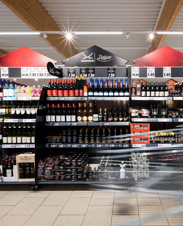 Ein Mann geht mit seinem Einkaufswagen in einer Lidl-Filiale an Regalen mit alkoholischen Getränken vorbei.