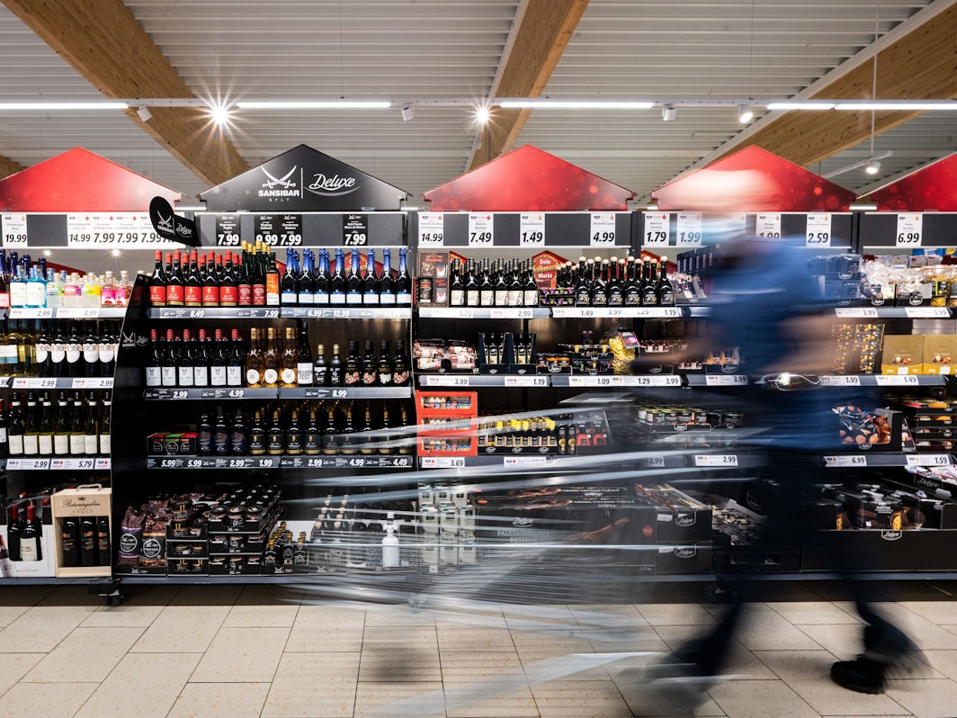 Ein Mann geht mit seinem Einkaufswagen in einer Lidl-Filiale an Regalen mit alkoholischen Getränken vorbei.