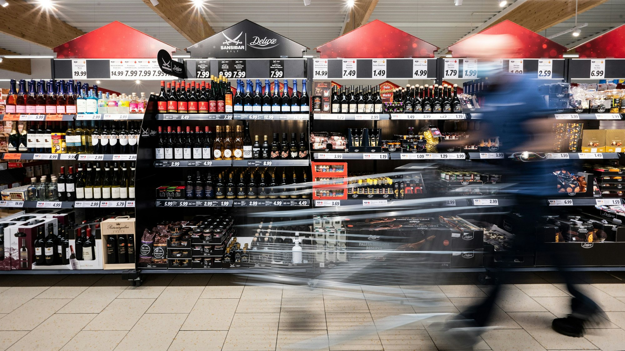 Ein Mann geht mit seinem Einkaufswagen in einer Lidl-Filiale an Regalen mit alkoholischen Getränken vorbei.