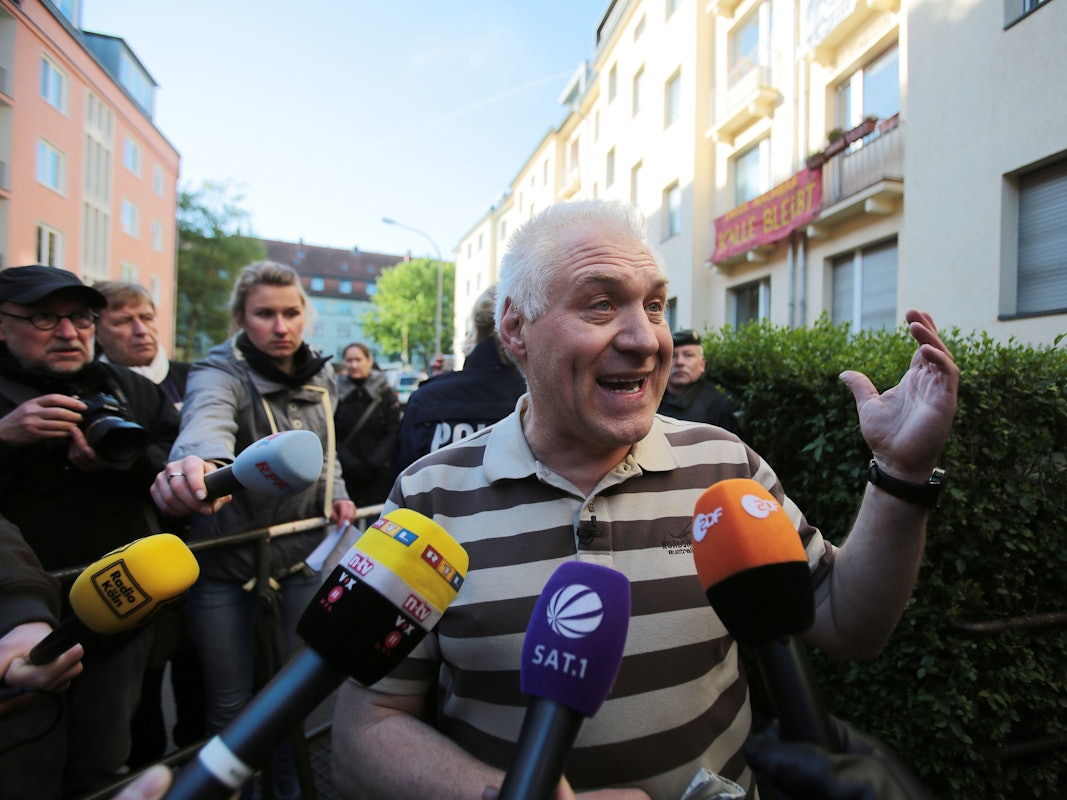 Ein Mann redet mit Journalisten, die Mikrofone halten.