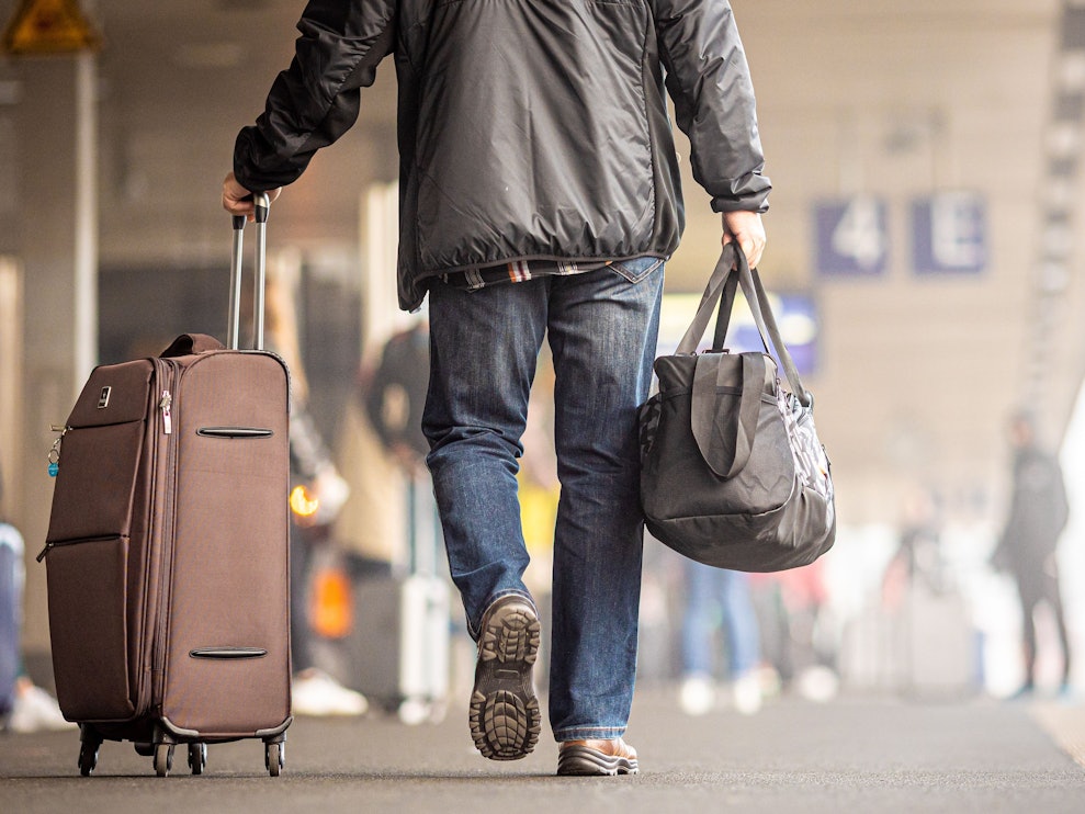 Ein Reisender geht mit seinem Koffer einen Bahnsteig entlang.