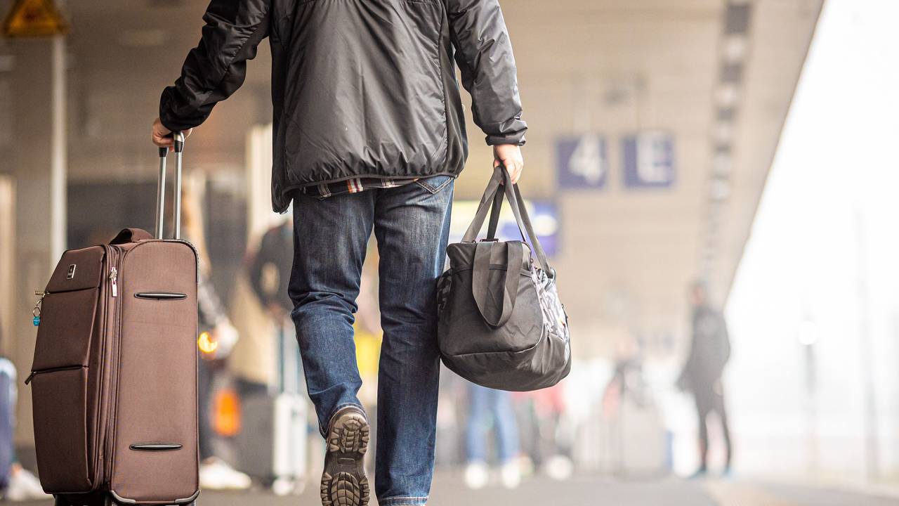 Ein Reisender geht mit seinem Koffer einen Bahnsteig entlang.