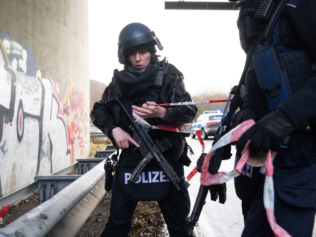 Zwei bewaffnete Polizeibeamte stehen mit Flatterband auf einer Straße.
