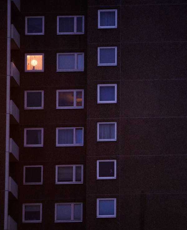 Eine Lampe brennt im Fenster eines Mehrfamilienhauses.