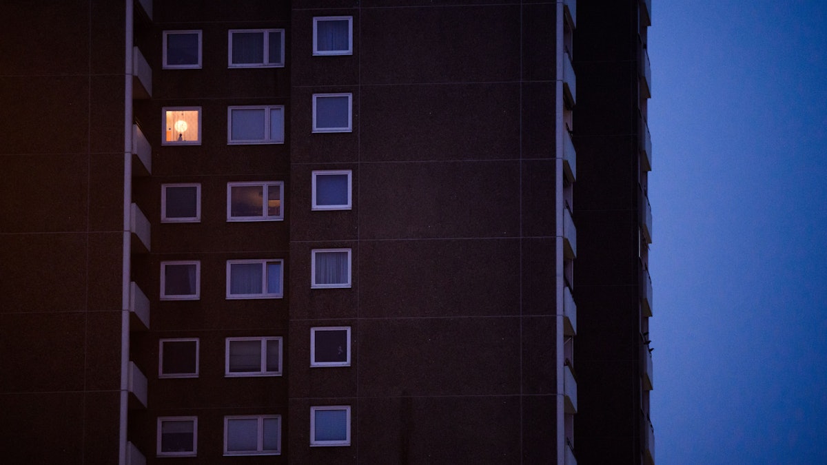 Eine Lampe brennt im Fenster eines Mehrfamilienhauses.