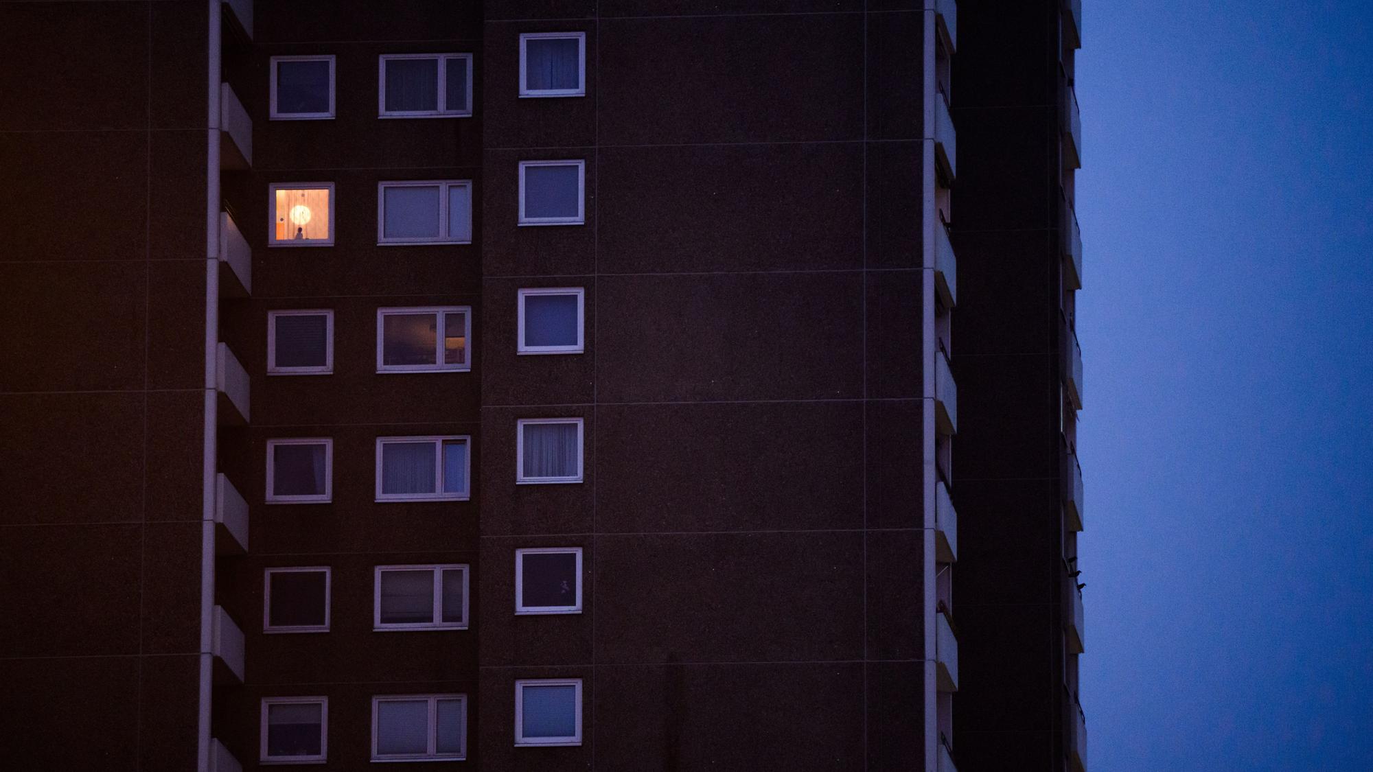Eine Lampe brennt im Fenster eines Mehrfamilienhauses.