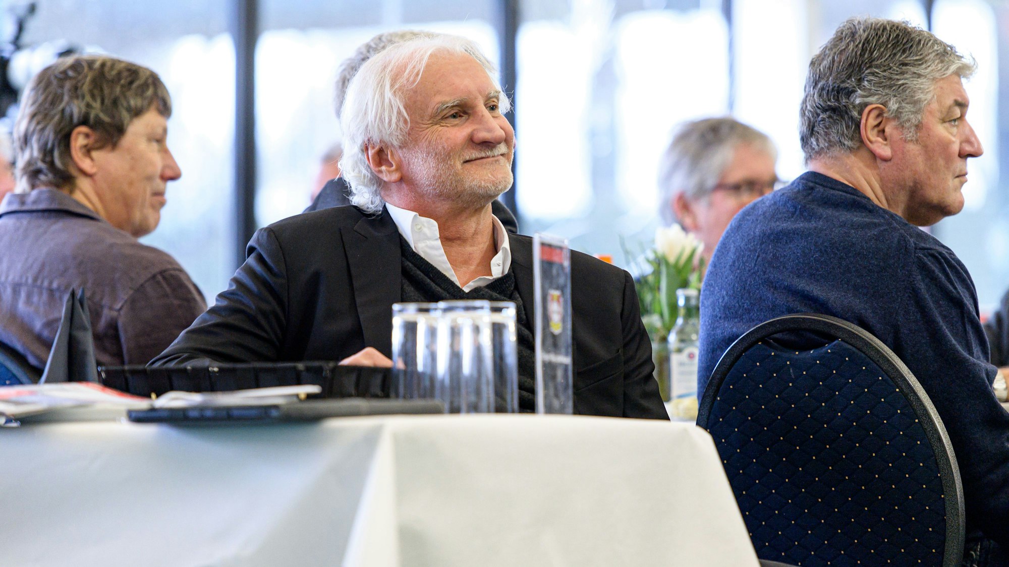 Rudi Völler sitzt am Tisch und hört zu.