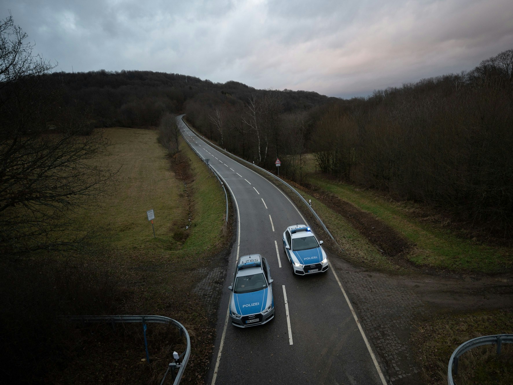 Polizeiwagen stehen an einer Absperrung an der Kreisstraße 22 rund einen Kilometer von dem Tatort, an dem ein Polizist und eine Polizeianwärterin durch Schüsse getötet wurden.