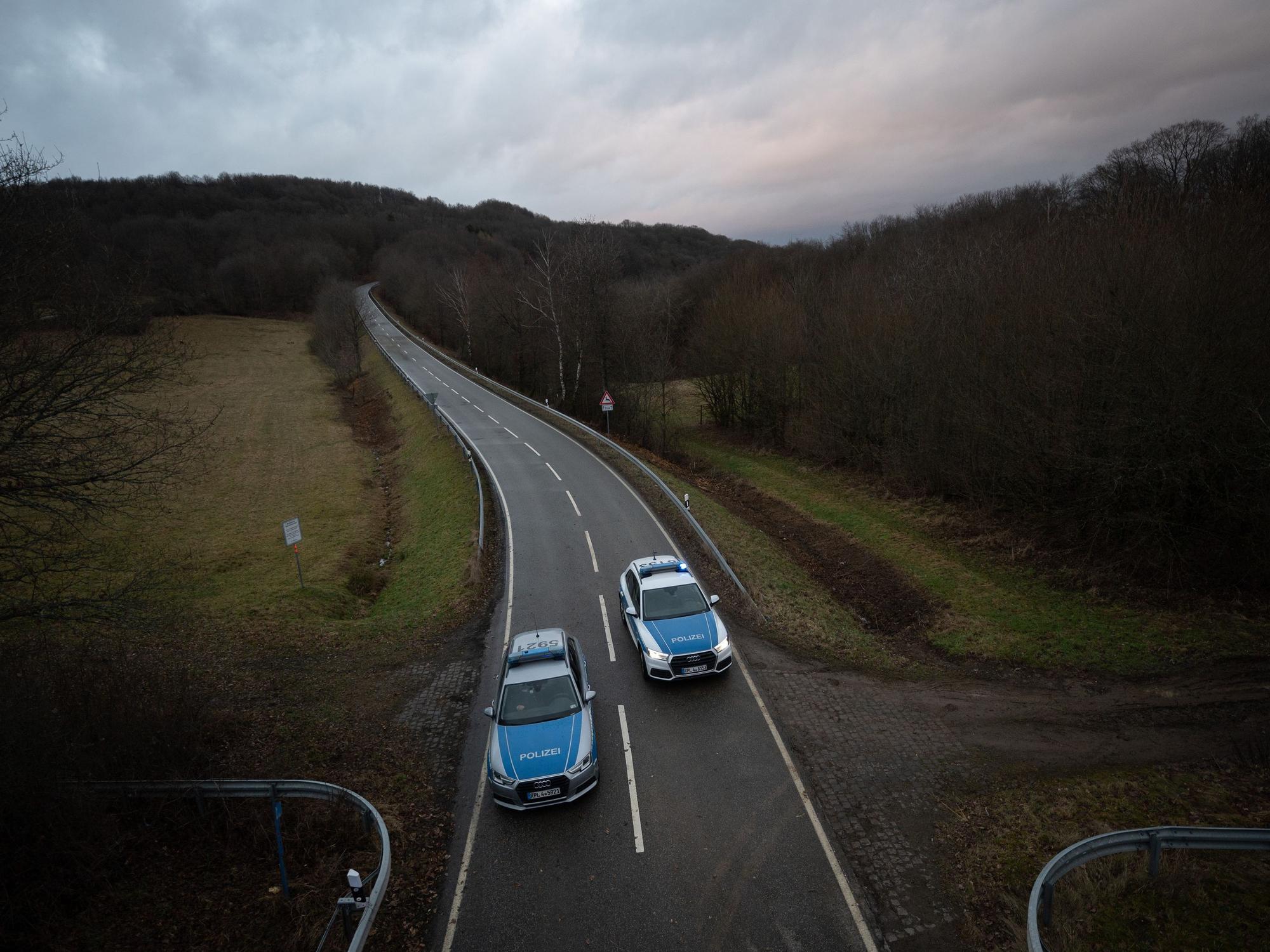 Zwei Polizeiwagen stehen an einer Absperrung an der Kreisstraße 22 rund einen Kilometer von dem Tatort, an dem zwei Polizeibeamte am 31. Januar 2022 durch Schüsse getötet wurden.