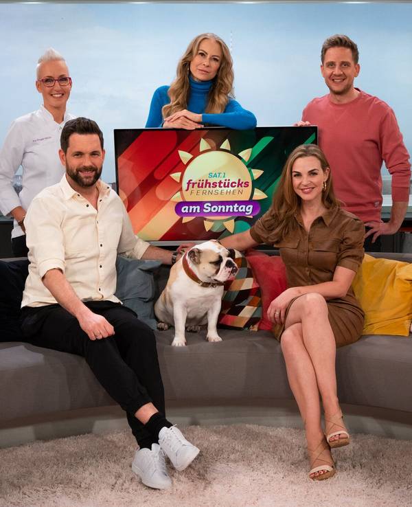 Matthias Killing und Annika Lau sitzen zusammen mit einem Hund auf dem Sofa. Ihre drei Kollegen stehen hinter dem Sofa.
