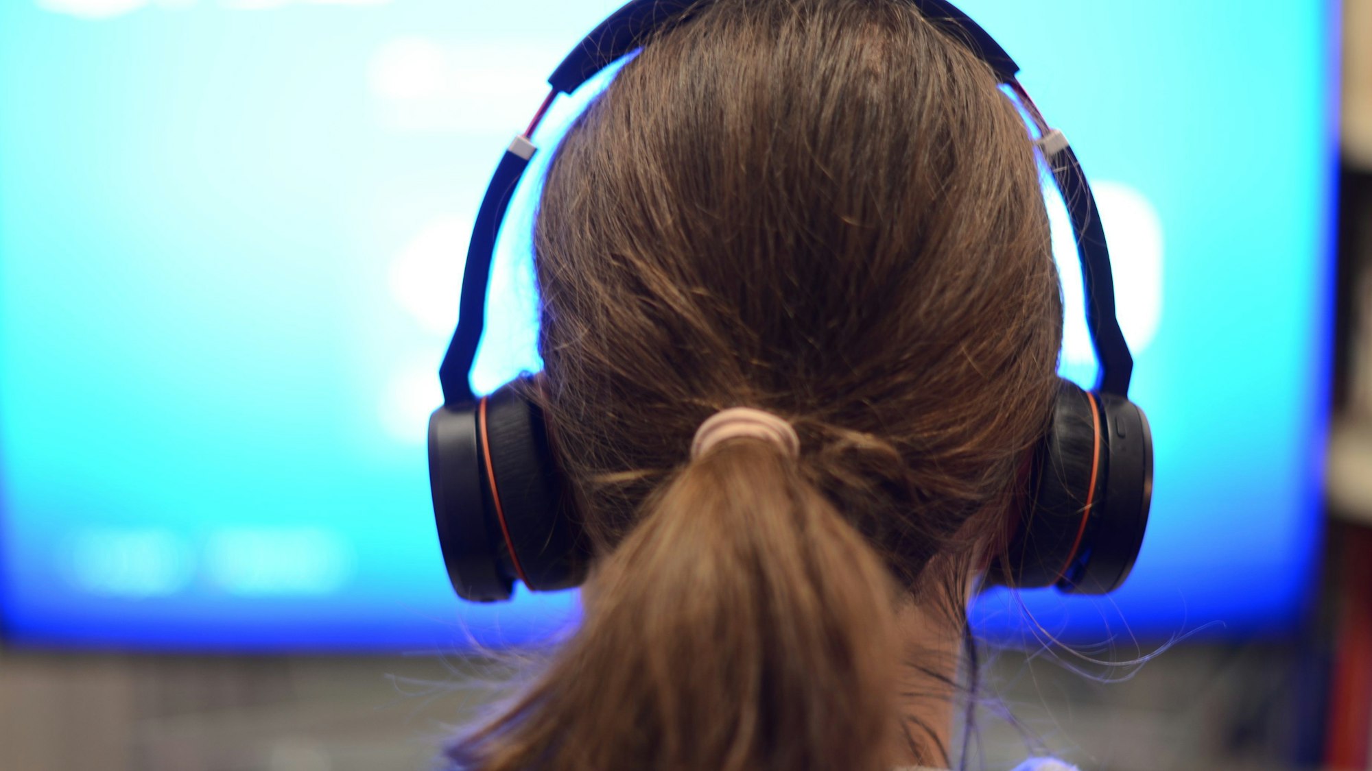 Eine Frau sitzt mit Kopfhörern vor einem Bildschirm.