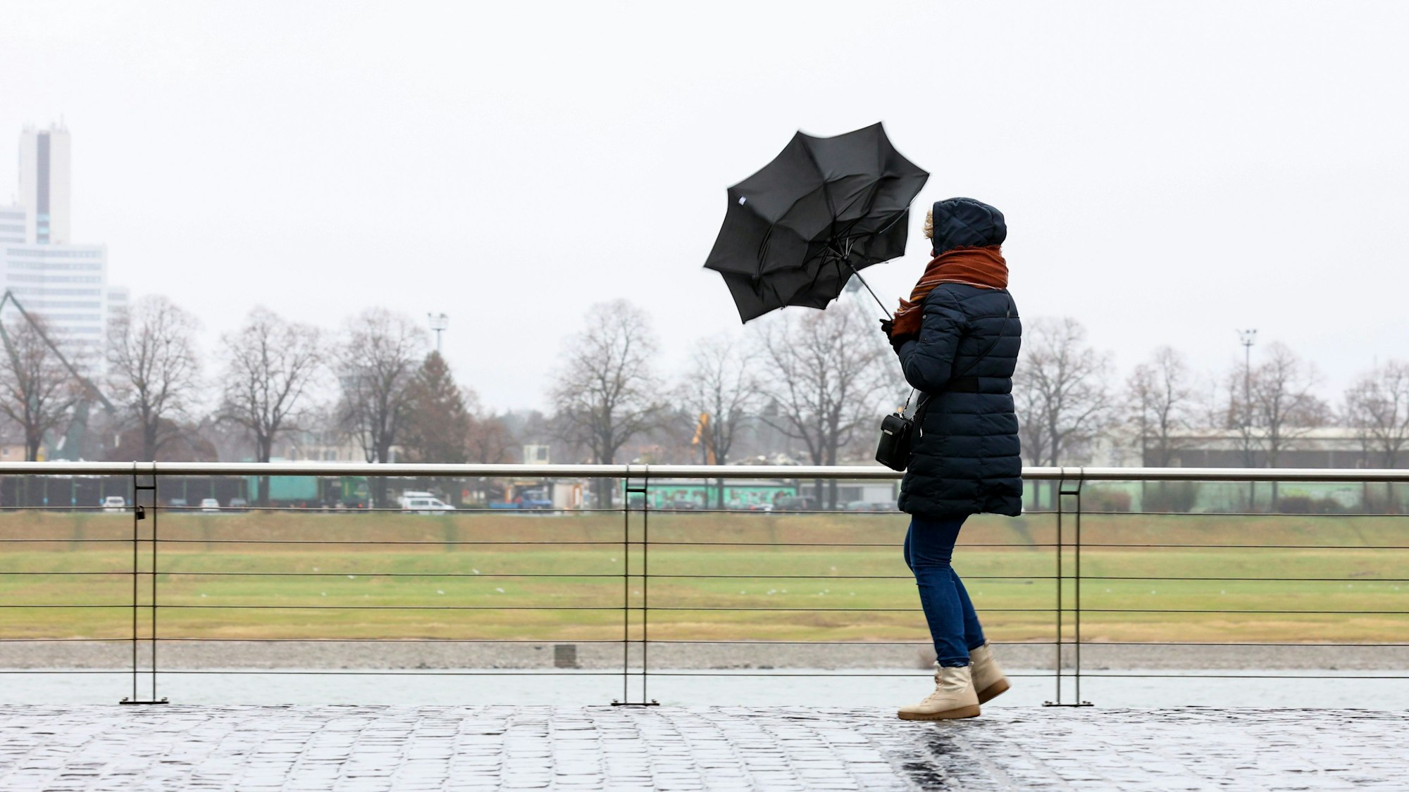 Im Rheinauhafen versucht eine Fußgängerin Ihren Schirm fest zu halten.