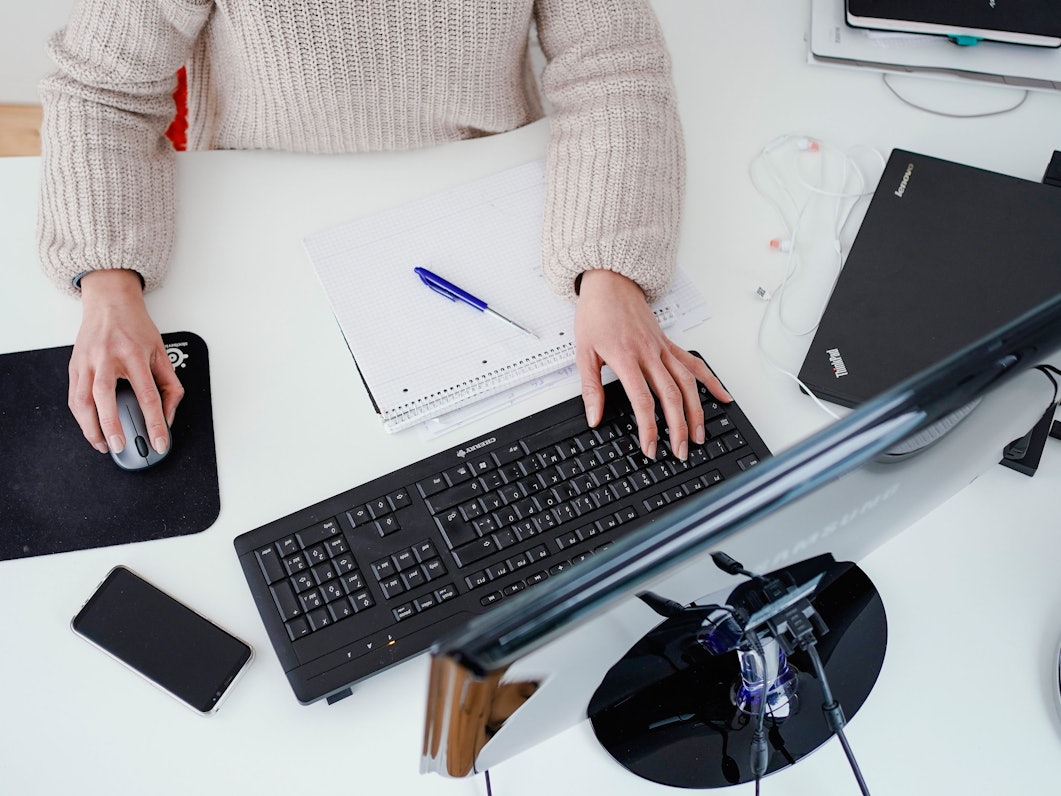 Eine Frau arbeitet in der Illustration an ihrem Schreibtisch: Sollte eine allgemeine Impfpflicht eingeführt werden, könnte es sein, dass Ungeimpfte nicht mehr beschäftigt werden können.