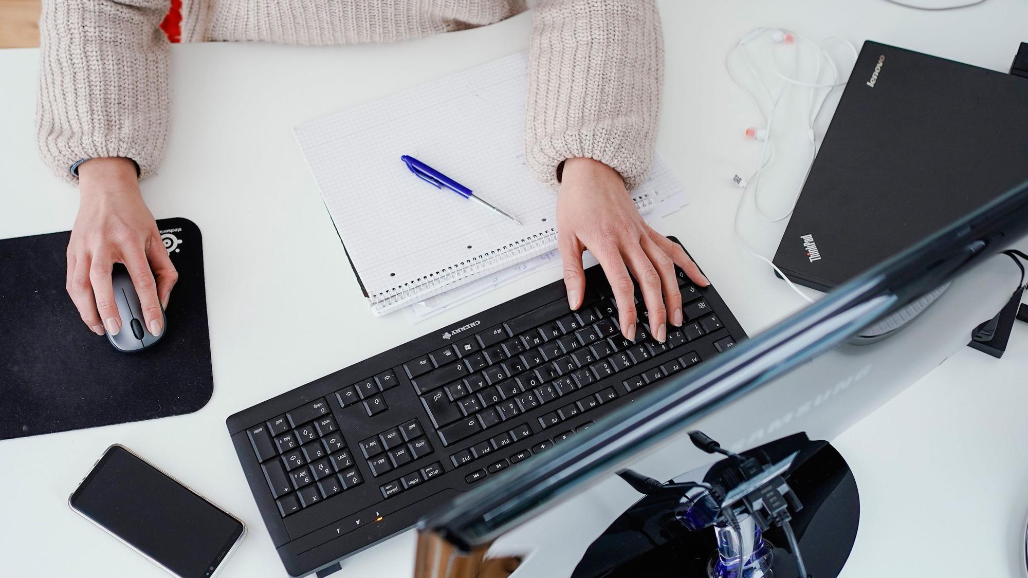 Eine Frau arbeitet in der Illustration an ihrem Schreibtisch: Sollte eine allgemeine Impfpflicht eingeführt werden, könnte es sein, dass Ungeimpfte nicht mehr beschäftigt werden können.