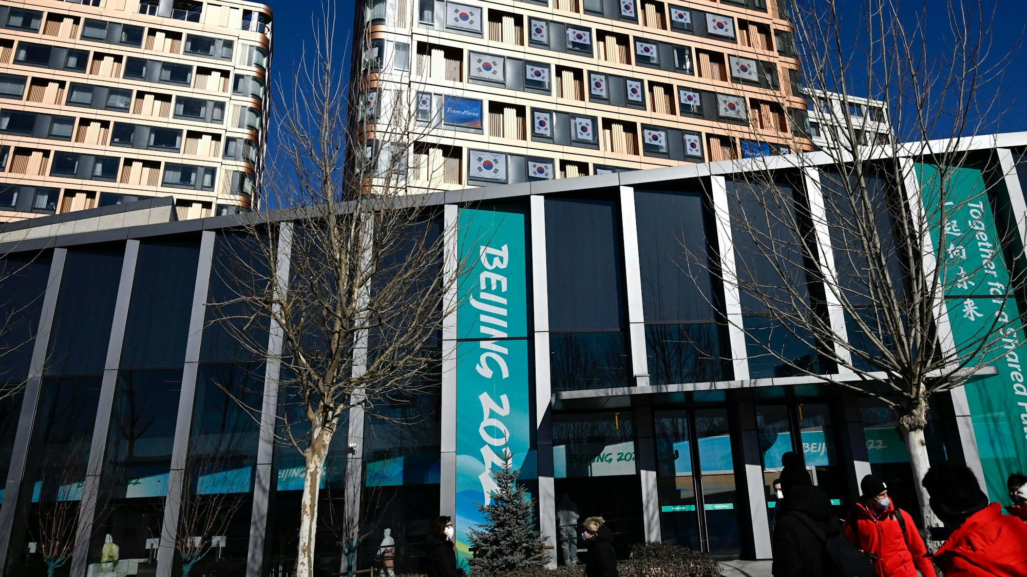 Menschen spazieren im Olympischen Dorf. Die Olympischen Winterspiele in Peking finden vom 4. bis 20. Februar 2022 unter strengen Corona-Auflagen statt.