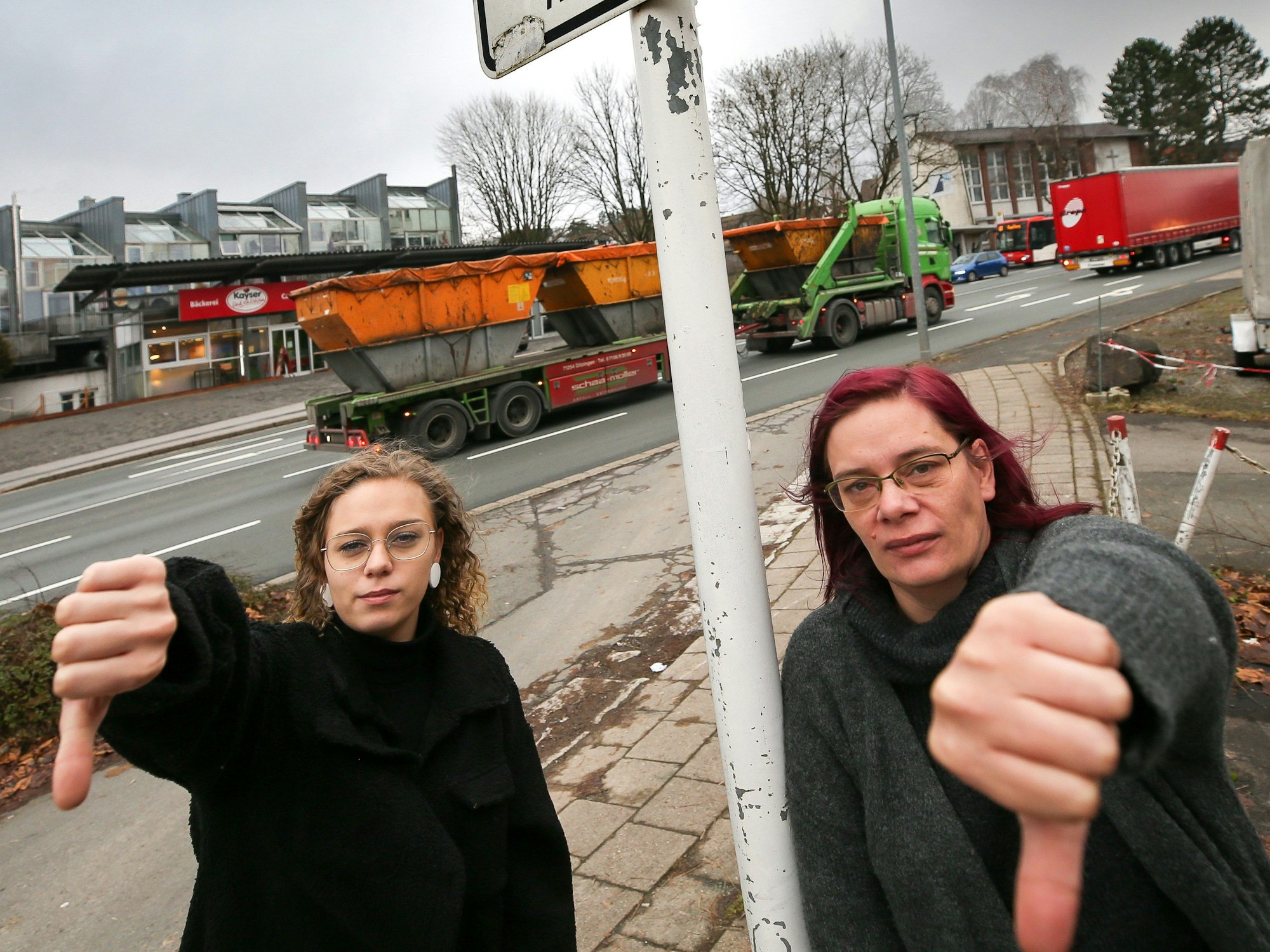 Zwei Frauen an einer Straße zeigen mit dem Daumen nach unten.
