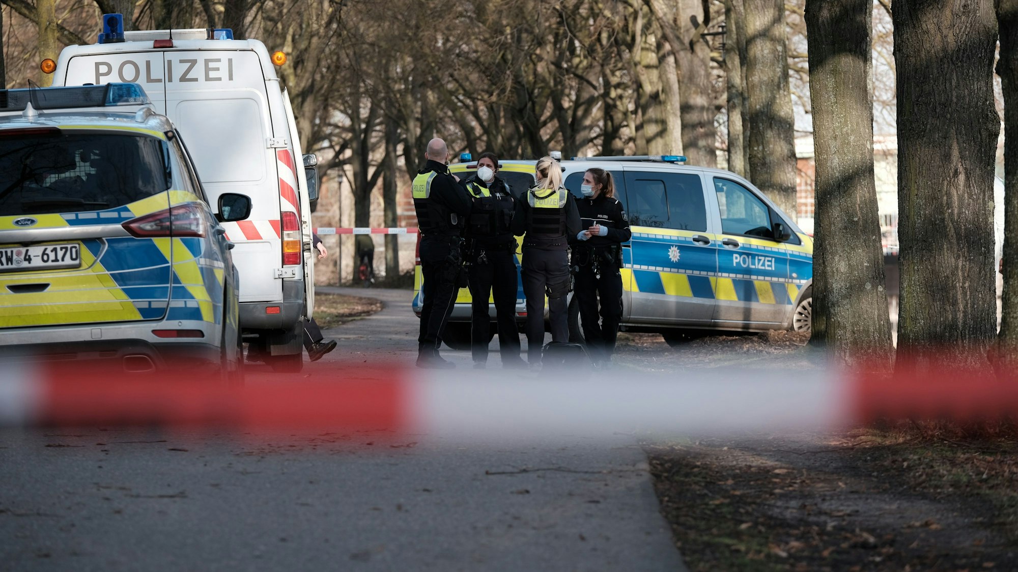 Drei Polizistinnen und ein Polizei stehen neben mehreren Polizeifahrzeugen innerhalb einer Absperrung.