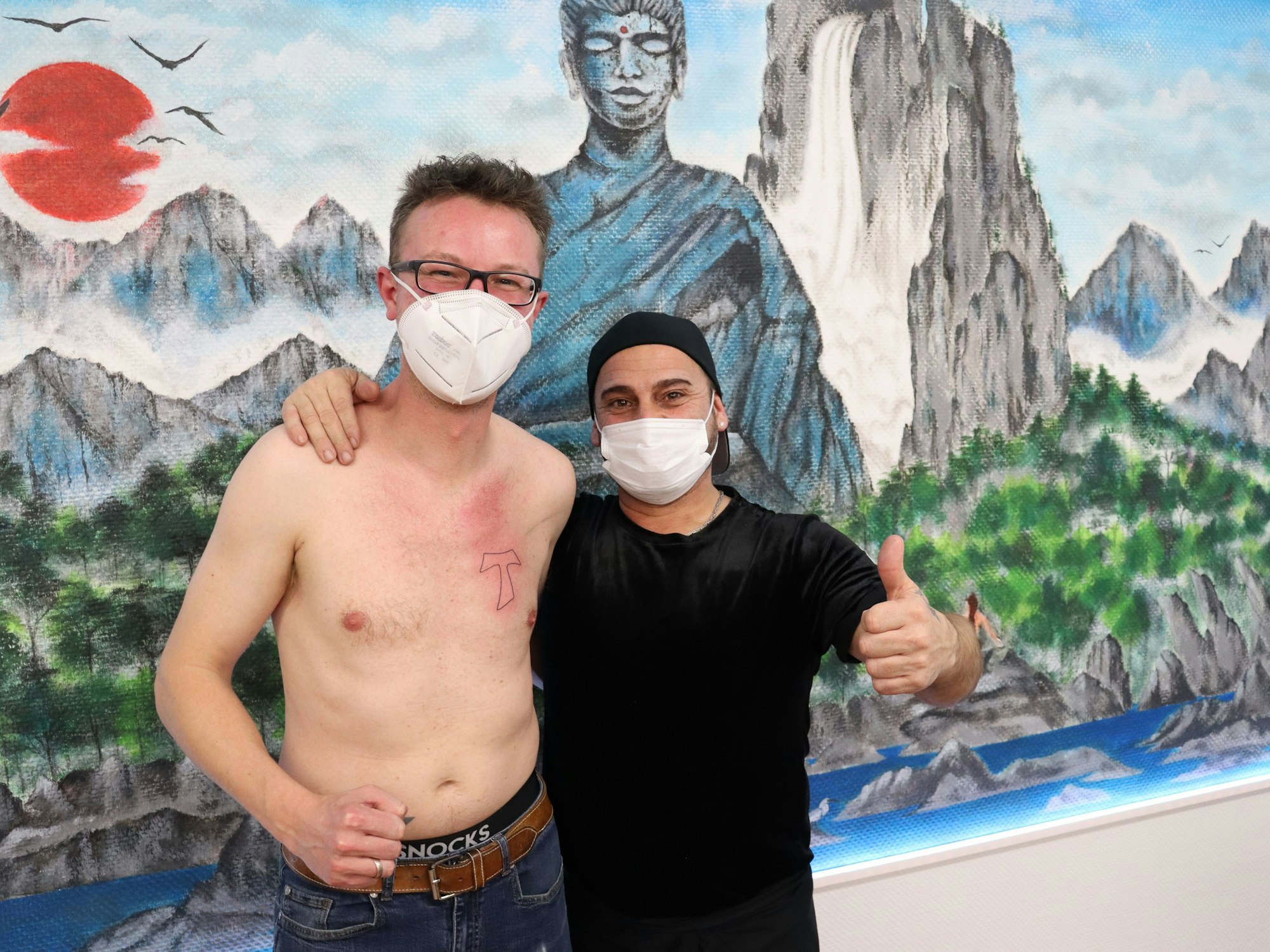 Sören Ahlhaus (l.) steht mit nacktem Oberkörper neben seinem Tätowierer Erkan. Beide zeigen einen Daumen hoch.