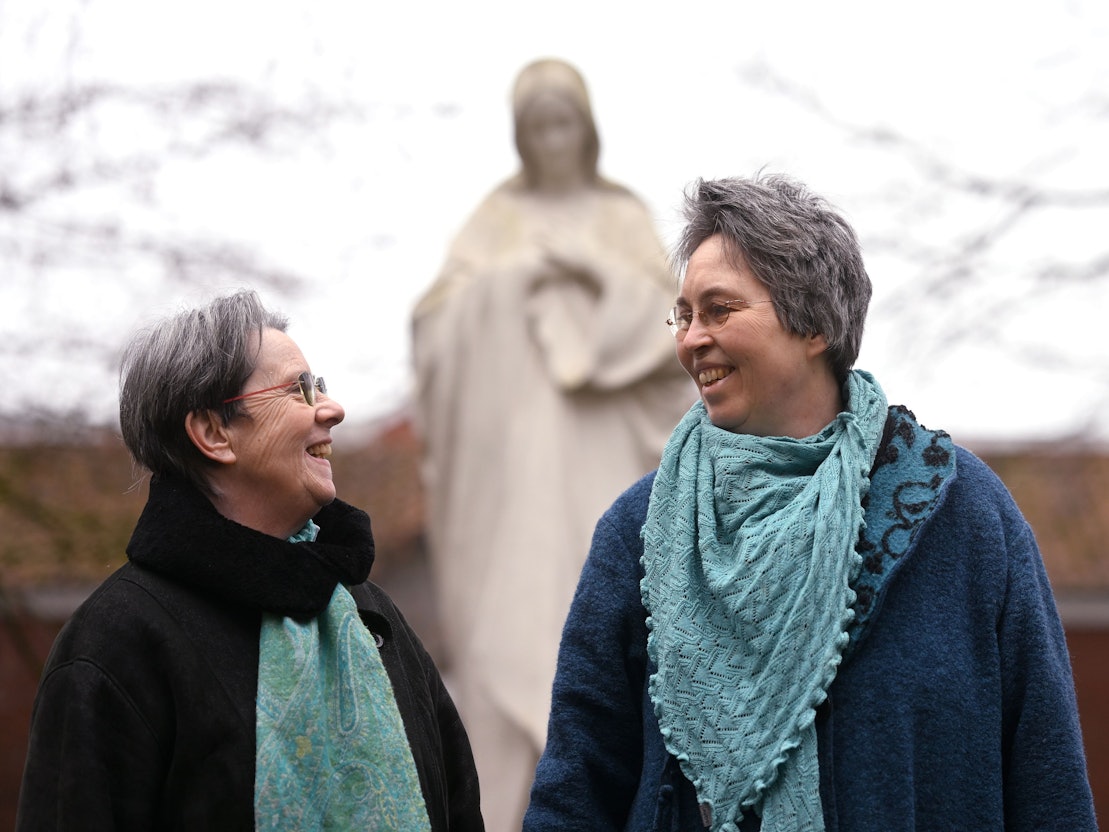 Queer in Church: Monika Schmelter (links) und Marie Kortenbusch vor einer Marienstatue eines Klosters. Die beiden sind ein Paar.