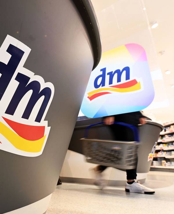 Eine Person geht in einer Filiale der Drogeriemarktkette dm mit einem Einkaufskorb am Kassenbereich vorbei.