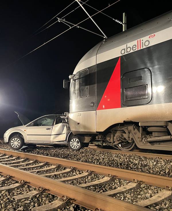 Ein Auto steht auf Gleisen vor einem Zug.