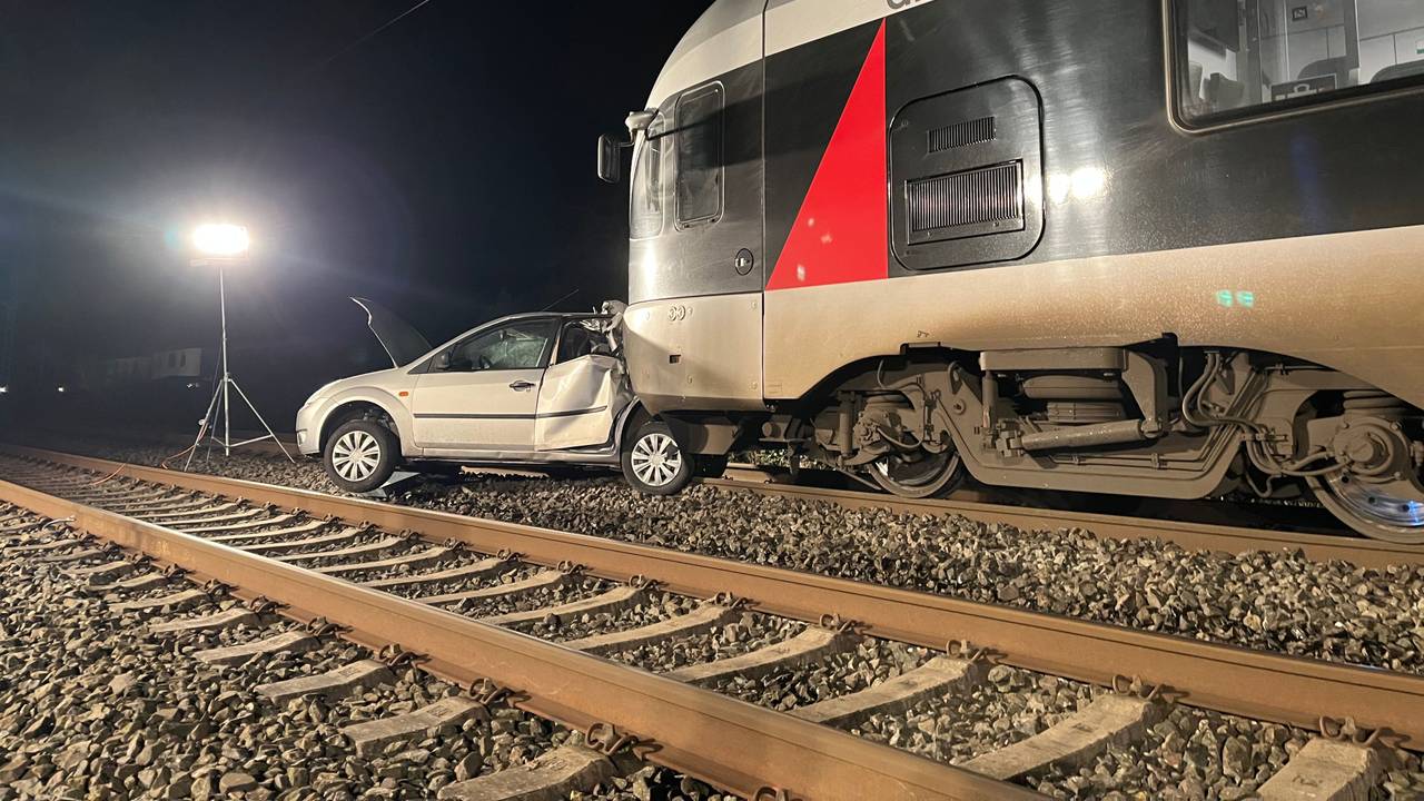 Ein Auto steht auf Gleisen vor einem Zug.