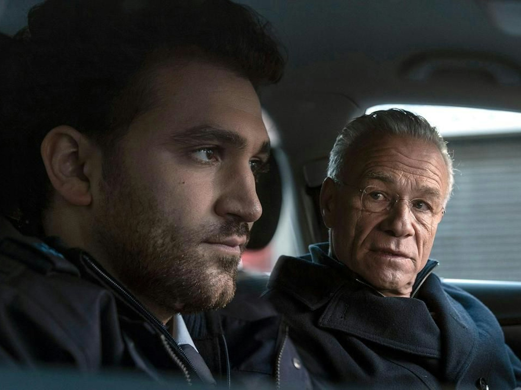 Zwei Männer sitzen in einem Auto während Filmaufnahmen.